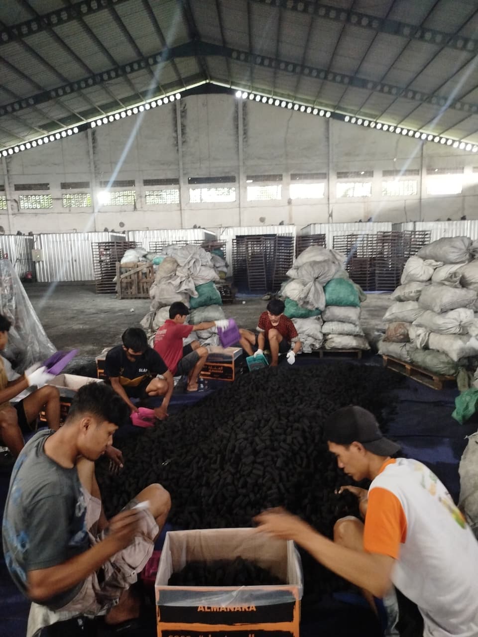 Workers manually sorting charcoal in a large warehouse